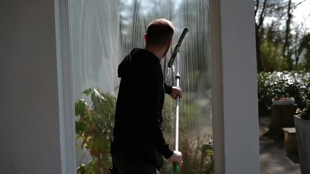 Eine hohe Fensterscheibe wird von innen mit einem Teleskopwerkzeug gereinigt.